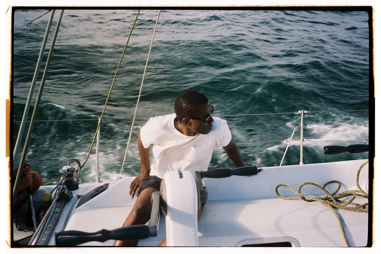 A crew member at the helm with a rough sea behind